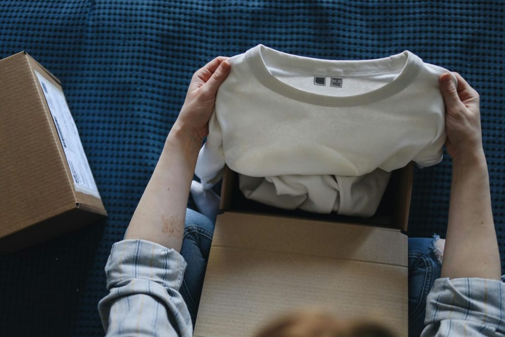 Close-up of hands opening a package containing a new white t-shirt indoors.